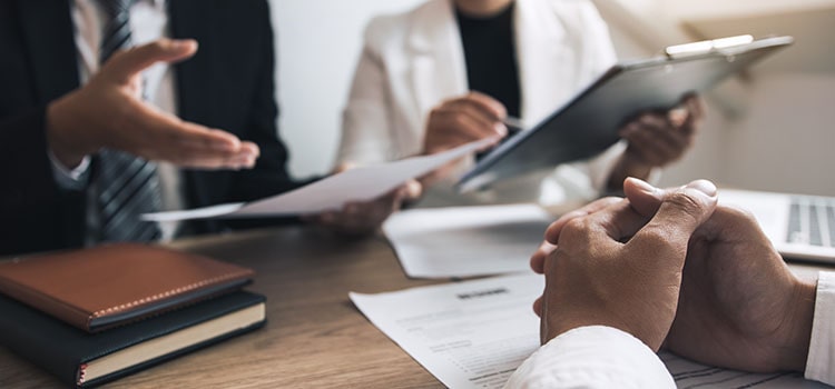 clasped hands over resume on desk while two interviewers discuss resume